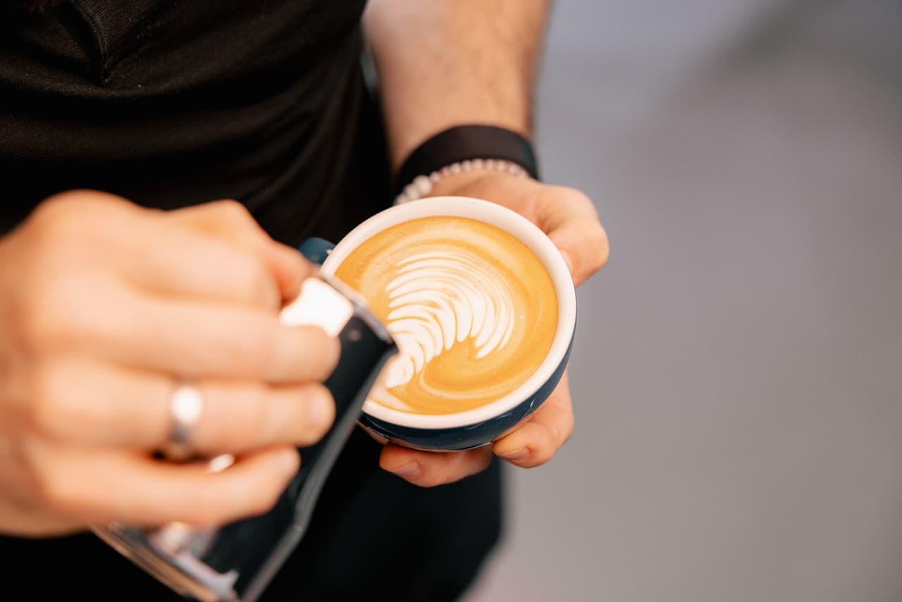 Barista gießt Milchschaum in kleine Espressotasse mit Latte Art – Heim-Espressomaschine, Espressozubereitung, Kaffee