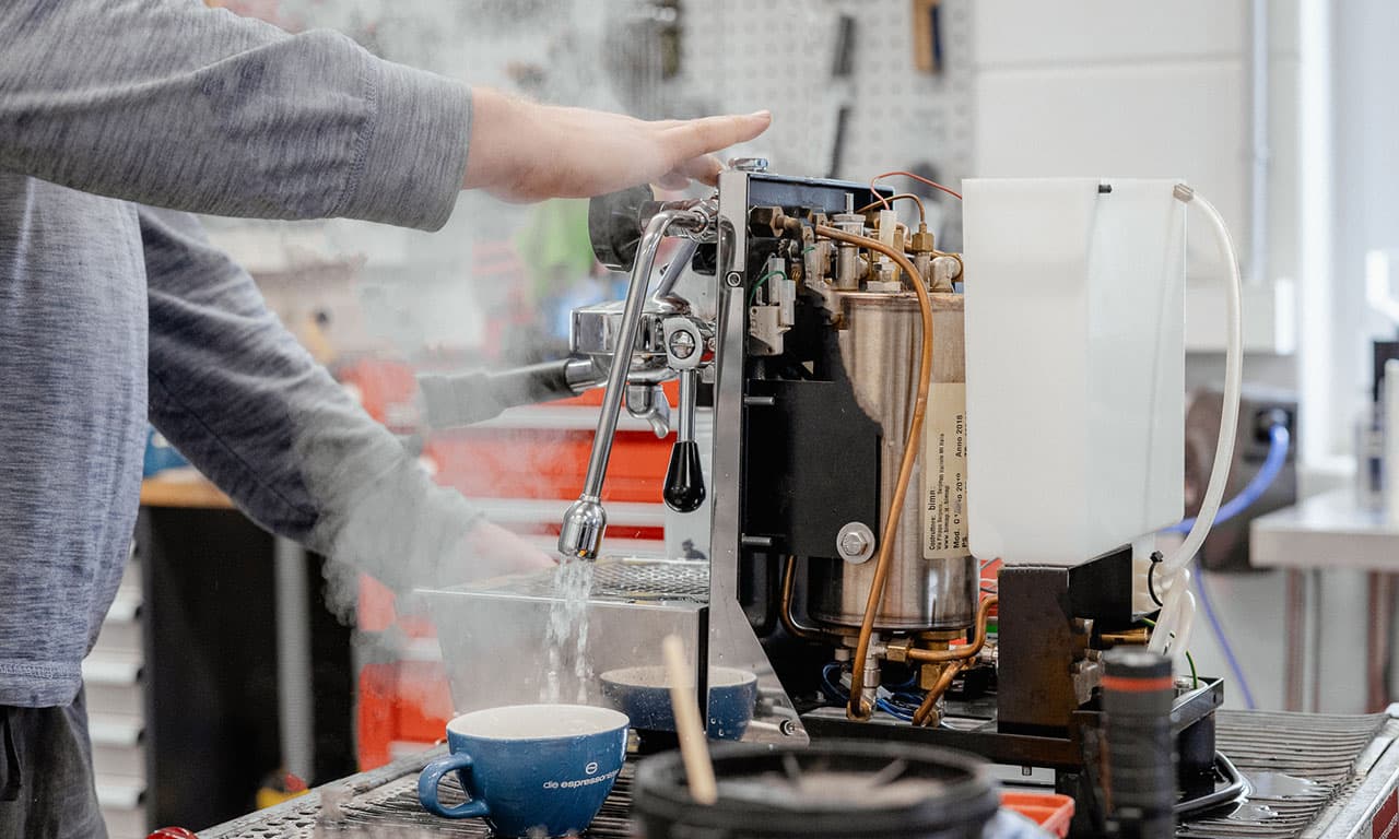 Techniker spült und überprüft offene Espressomaschine bei Wartung, Dampf, Wasserlauf und sichtbare Innenkomponenten