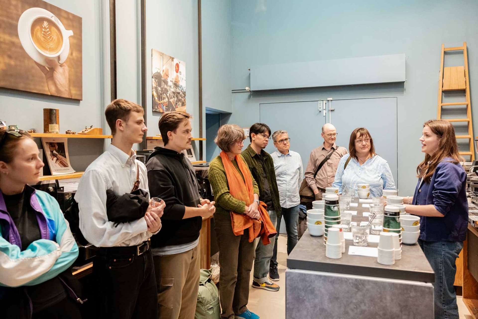 Gruppe von Menschen steht an einer Bar während einer Kaffee‑Verkostung; Barista erklärt Tassen und Kaffeebecher (La Bohème Takeover)