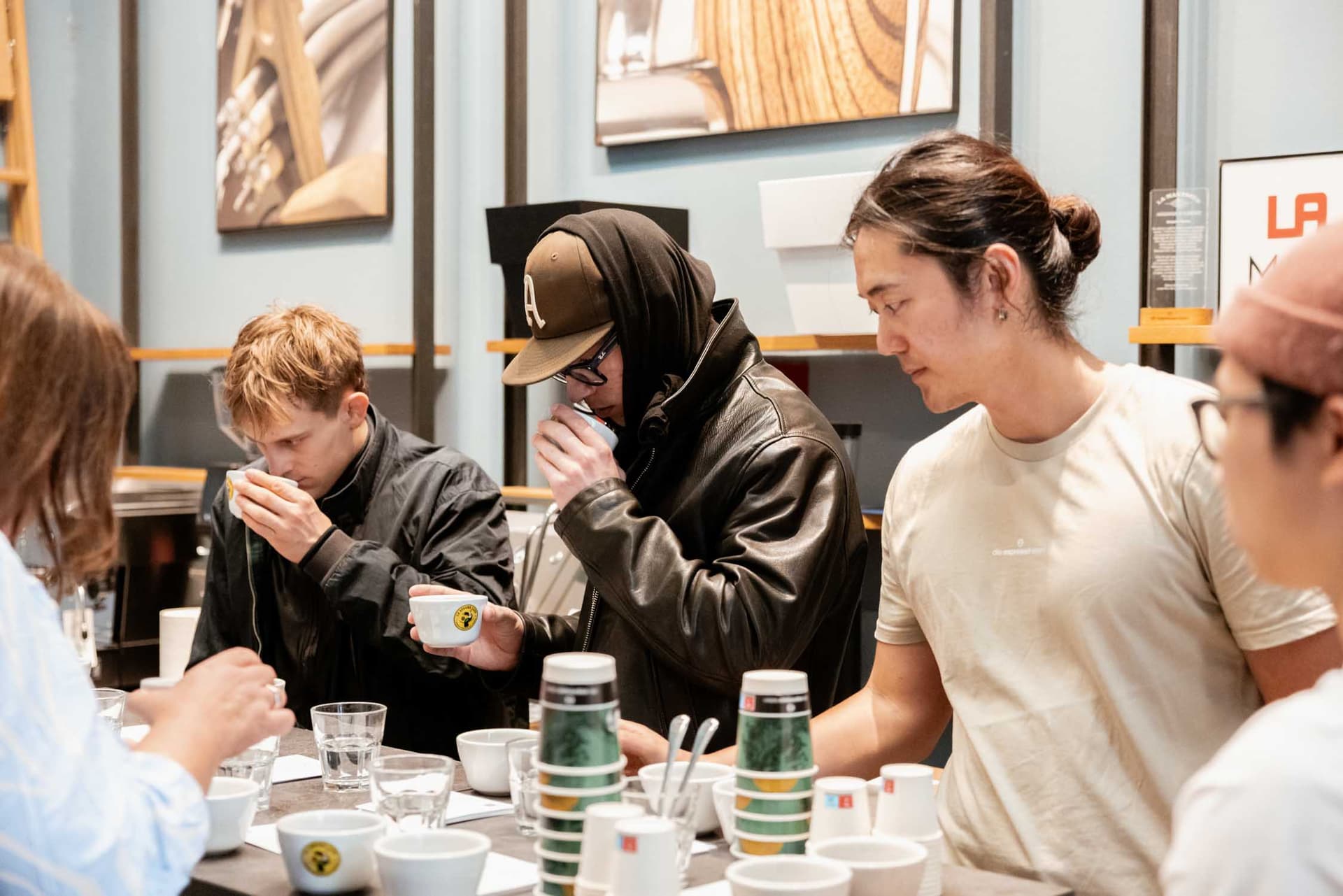 Barista-Takeover: mehrere junge Menschen verkosten Kaffee an einer Bar mit Tassen und Kaffeebecher-Stapel