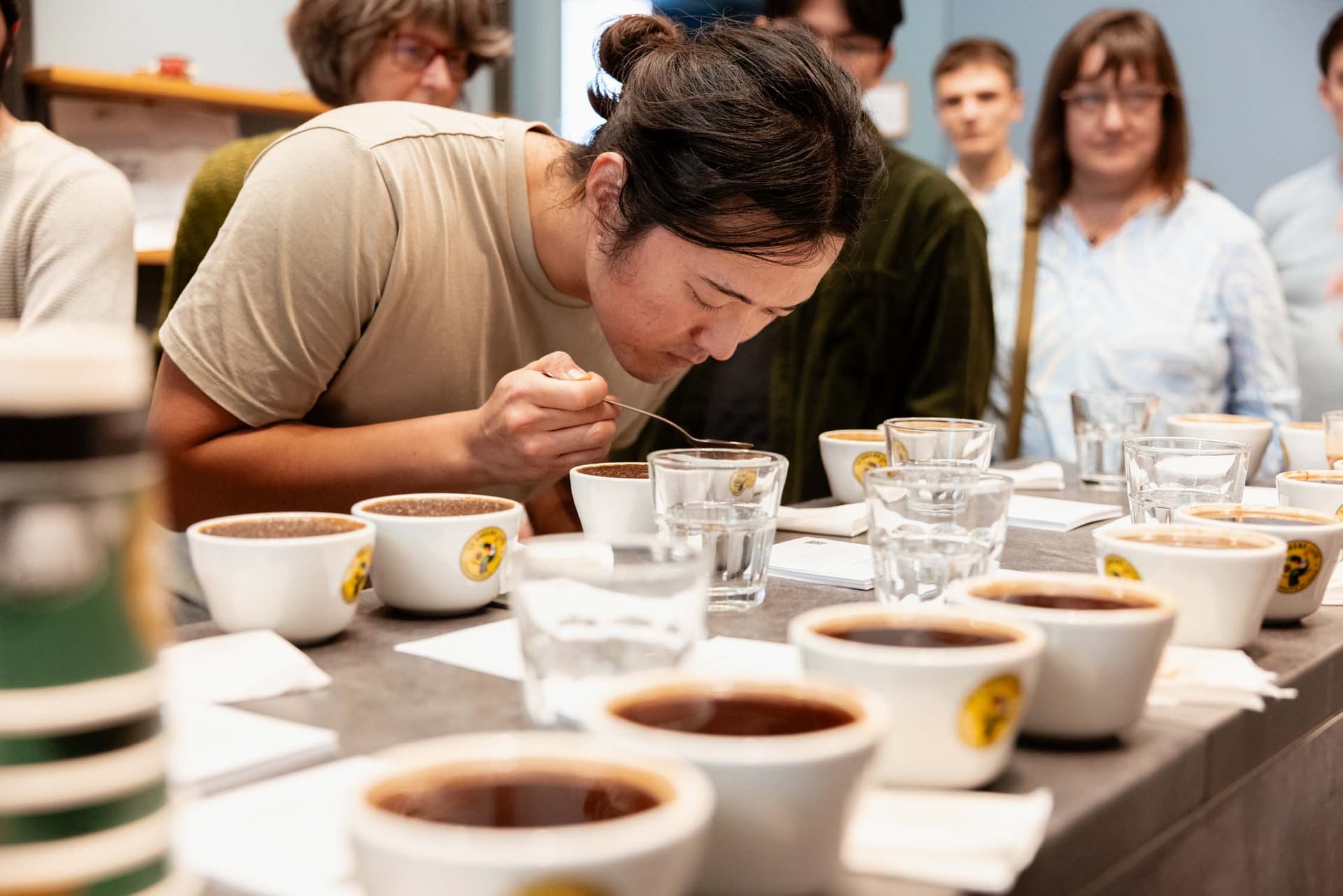 Barista riecht konzentriert an verschiedenen Kaffeetassen beim Cupping-Tasting, Kaffeetassen und Wassergläser auf Tisch